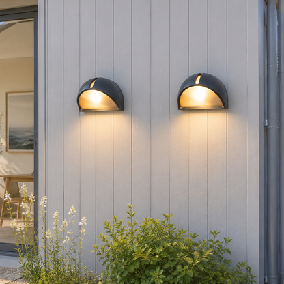 Two outdoor wall lights on a house exterior with plants and a sliding glass door in the background.